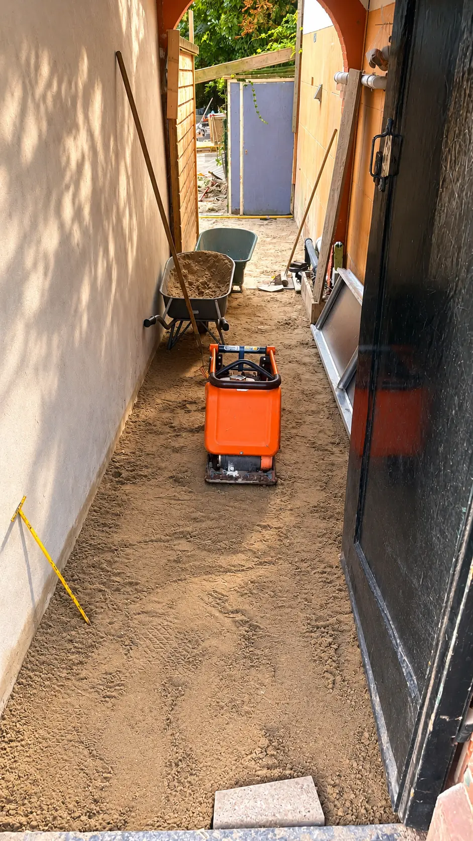 Nieuw zandbed wordt verdicht met een trilplaat in een doorgang bij Hotel Satori Amsterdam